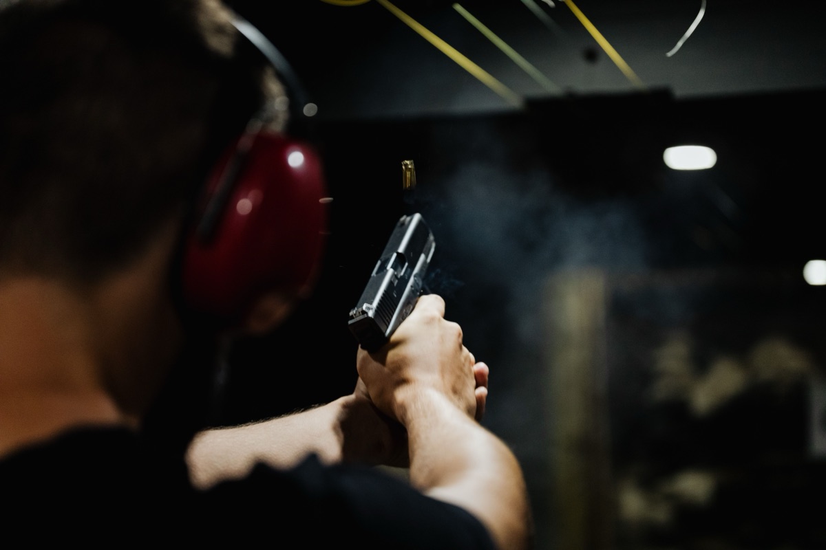 Live fire at an indoor range — brass in the air and muzzle smoke: the half-second airsoft never gets to teach you