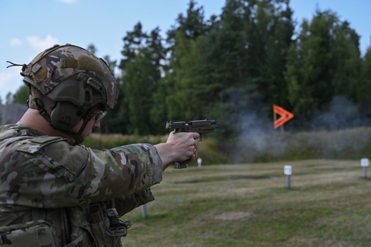 身穿迷彩的士兵在戶外考核靶場以 M17 手槍射擊