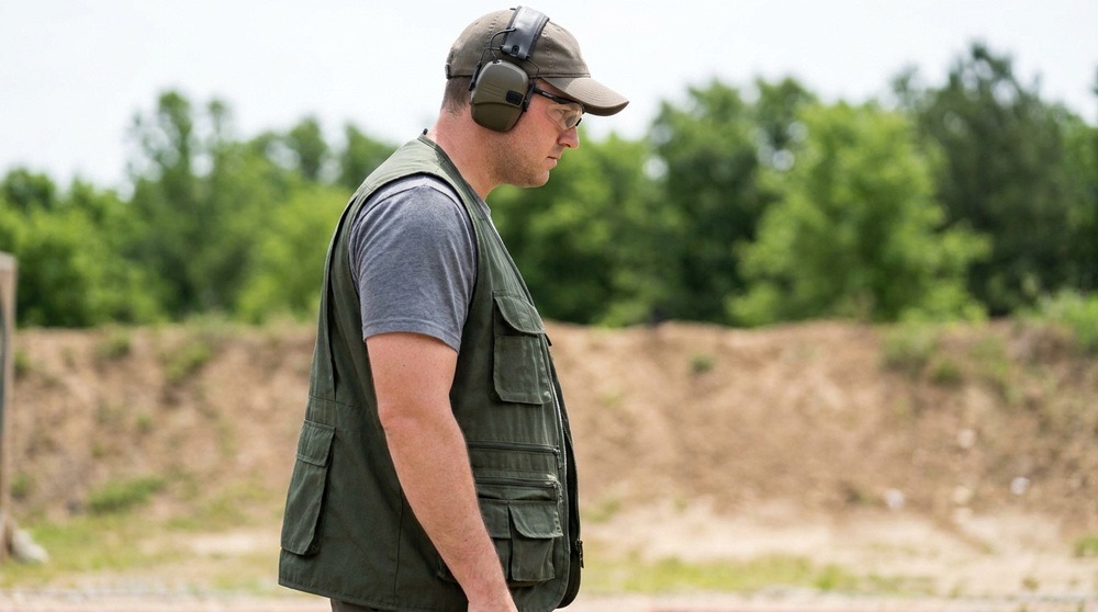 A competitor in an open-front shooting vest, the hem covering the beltline so that holster and magazine carriers are not visible from the side — the concealment that IDPA 8.6.2.3 and 8.7.1 require (AI-generated illustration)