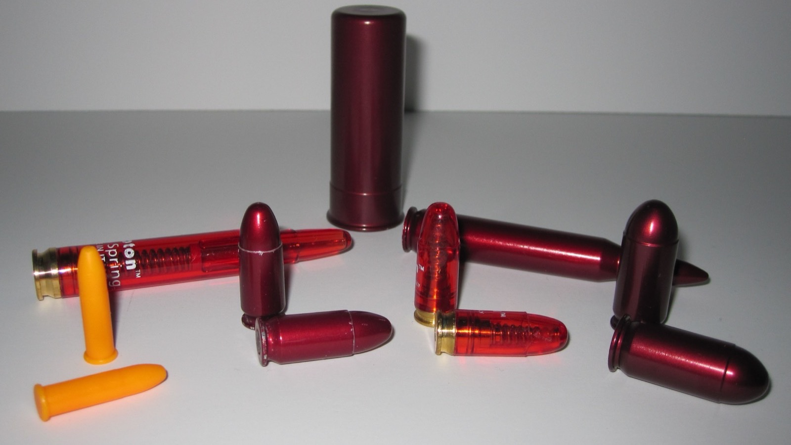 Inert snap caps in several calibers, including orange plastic .22 dummies and red aluminium pistol and rifle dummies, used for ball-and-dummy practice