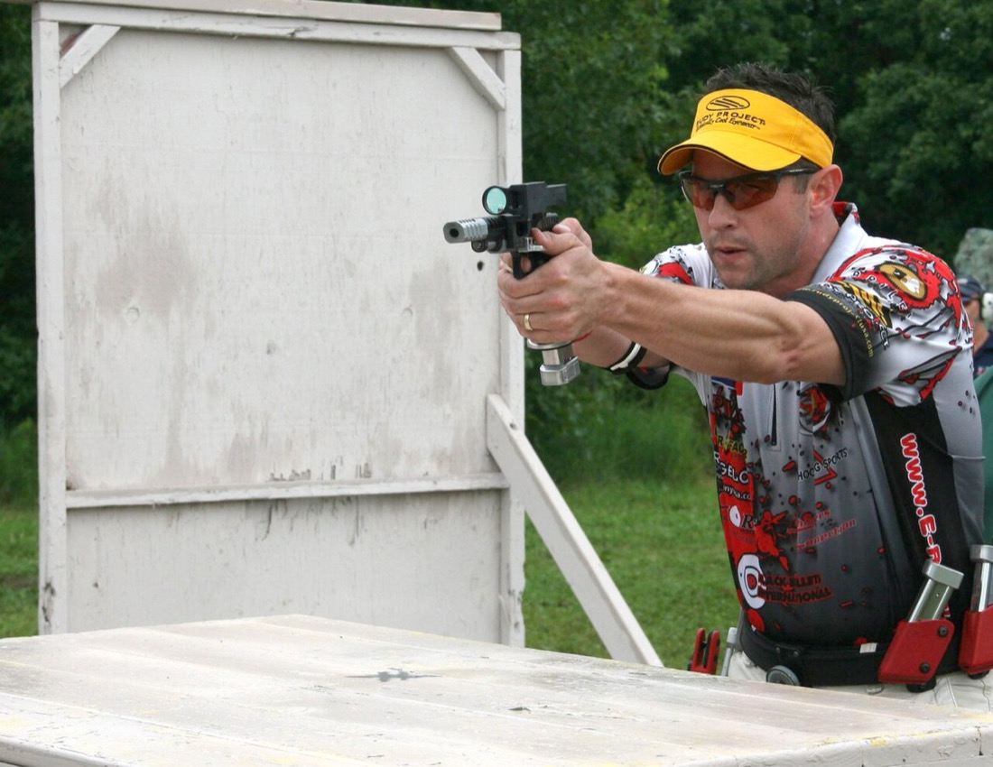A competitor shooting from behind a wooden barricade — the body stays behind the cover line while the gun works around the edge