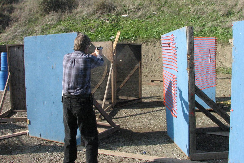 A shooter working a match stage between plywood barricades, with wooden boards on the ground marking the shooting area
