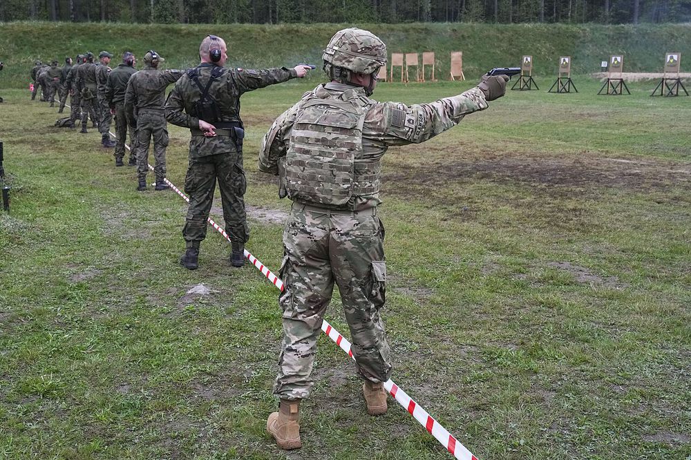 Soldiers firing pistols with one arm extended during a one-handed pistol event; the shooter in front keeps his free hand tucked behind his back