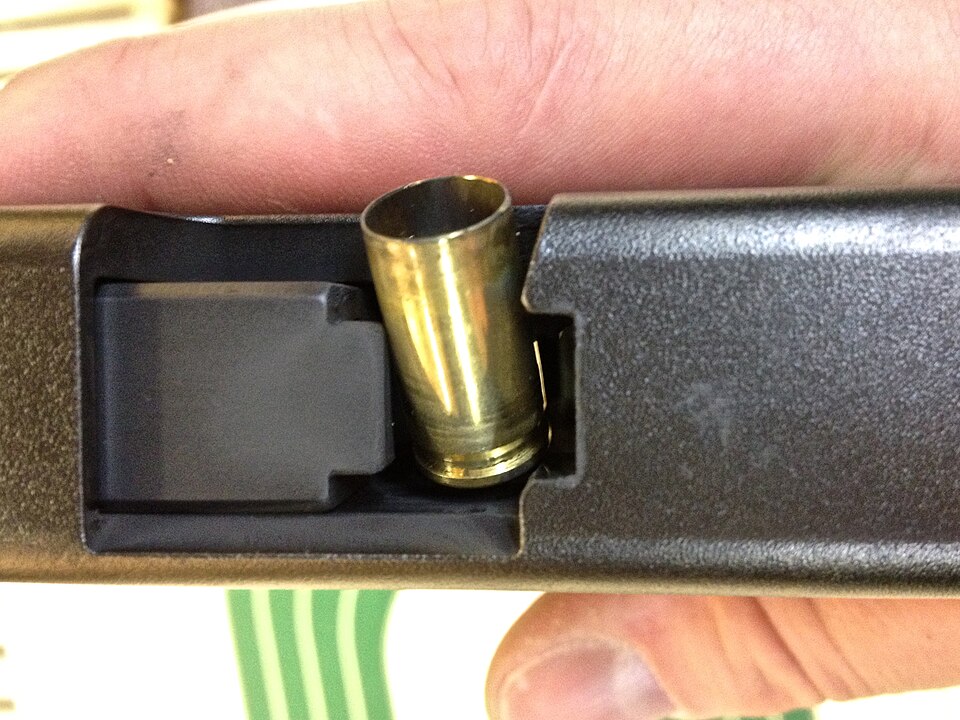 射手手持手槍的特寫，一枚空彈殼卡在拋殼口形成「煙囪」故障