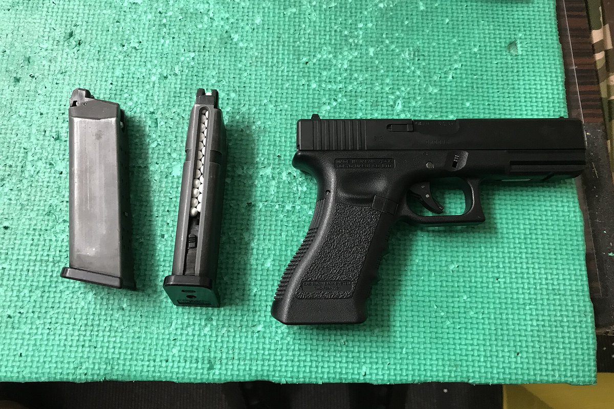 Tokyo Marui Glock 17 gas blowback airsoft pistol beside two magazines, one loaded with white BBs, on a shooting bench mat
