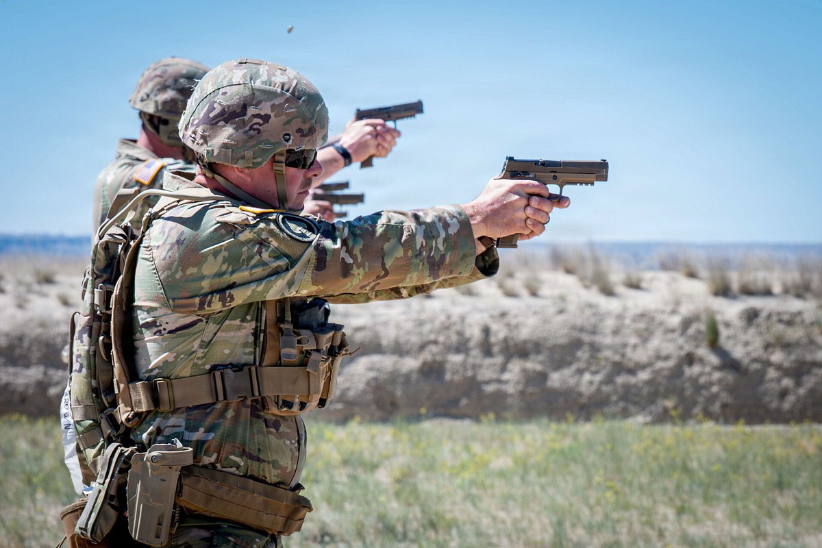 National Guard soldiers in helmets and eye protection firing M17 pistols with both arms extended during a pistol close-quarters battle course on an outdoor range