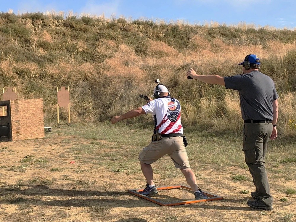 USPSA 比賽中射手在起始框內接戰標靶，Range Officer 拿著射擊計時器跟在身後——計時器是每一個 classifier 成績的一半